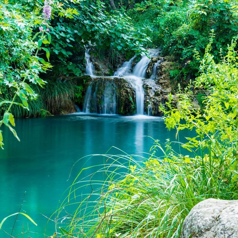 Serene view of Polylimnio Waterfalls in Messinia, Greece, showcasing cascading crystal-clear waters through lush greenery, a hidden gem for nature enthusiasts and hikers.