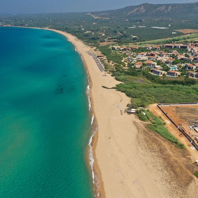 Stunning view of Romanos Beach in Messinia, Greece, with its expansive golden sands, crystal-clear azure waters, and picturesque sunsets, ideal for relaxation and water sports.