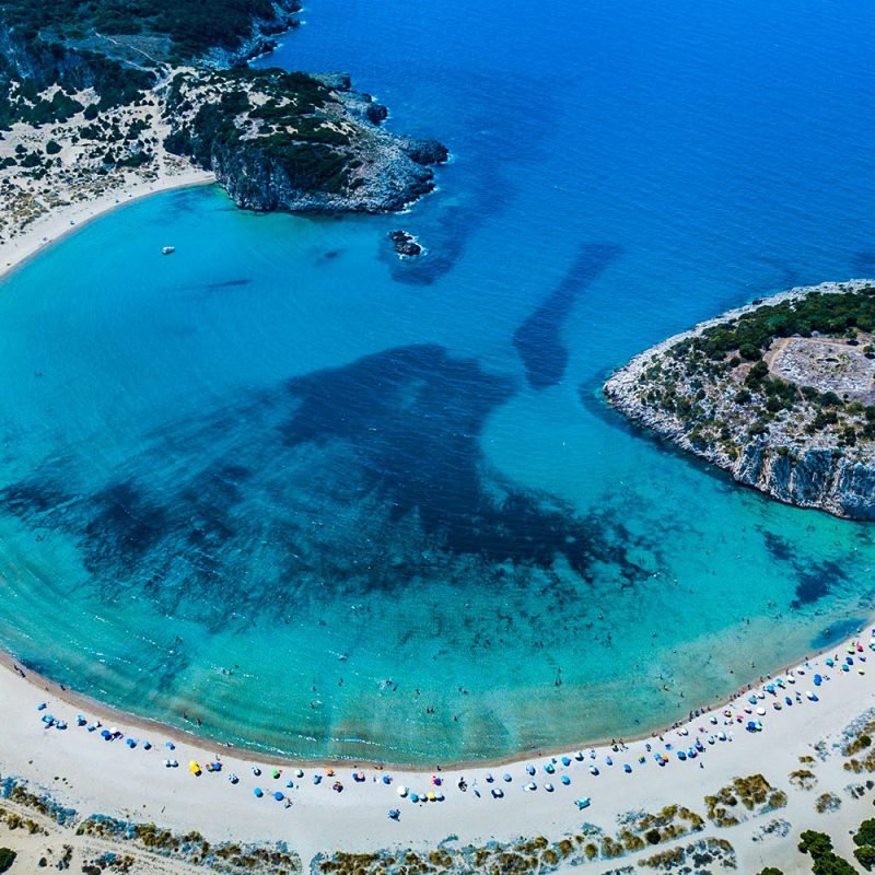 Panoramic view of Voidokilia Beach, a top-rated destination in Messinia, Greece, showcasing its distinctive omega-shaped coastline, pristine golden sands, and crystal-clear azure waters, ideal for swimming and nature photography.